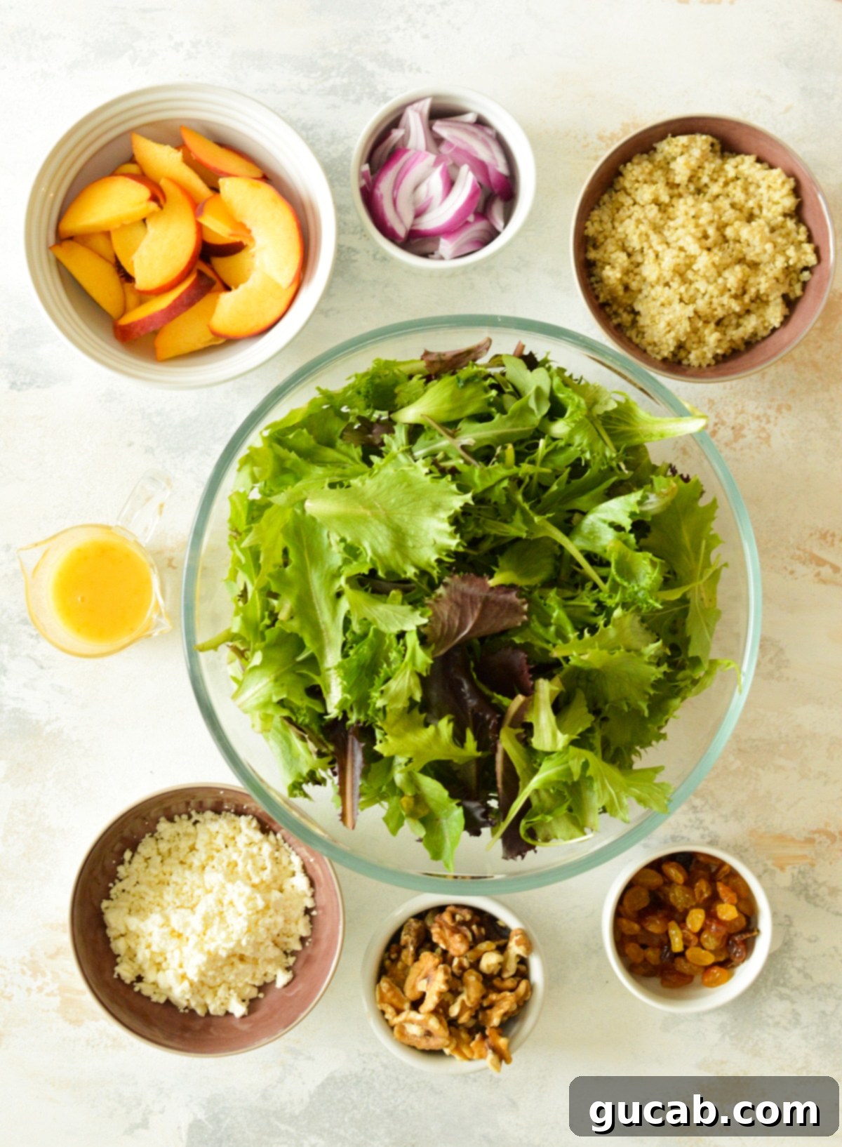 Peachy Feta Quinoa Salad 3 A flat lay image displaying all the fresh ingredients for a healthy lemon quinoa salad with peaches, including vibrant mixed greens, juicy peaches, crunchy walnuts, sweet golden raisins, creamy feta cheese, fluffy cooked quinoa, and thinly sliced red onion, alongside the components for the homemade dressing.