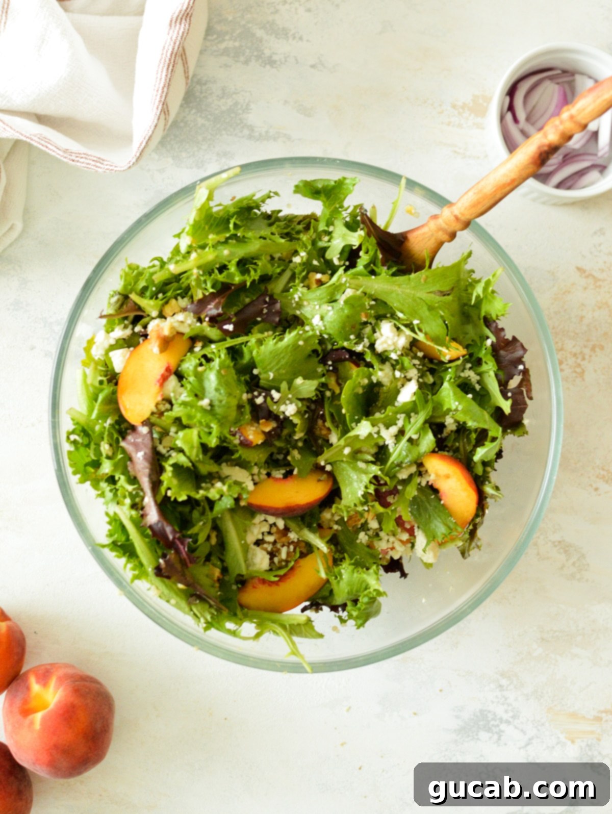 Peachy Feta Quinoa Salad 5 A close-up view of a vibrant and perfectly tossed Quinoa Salad with Feta and Peaches, featuring mixed greens, quinoa, feta, peaches, and red onion, all glistening with dressing and ready to serve.