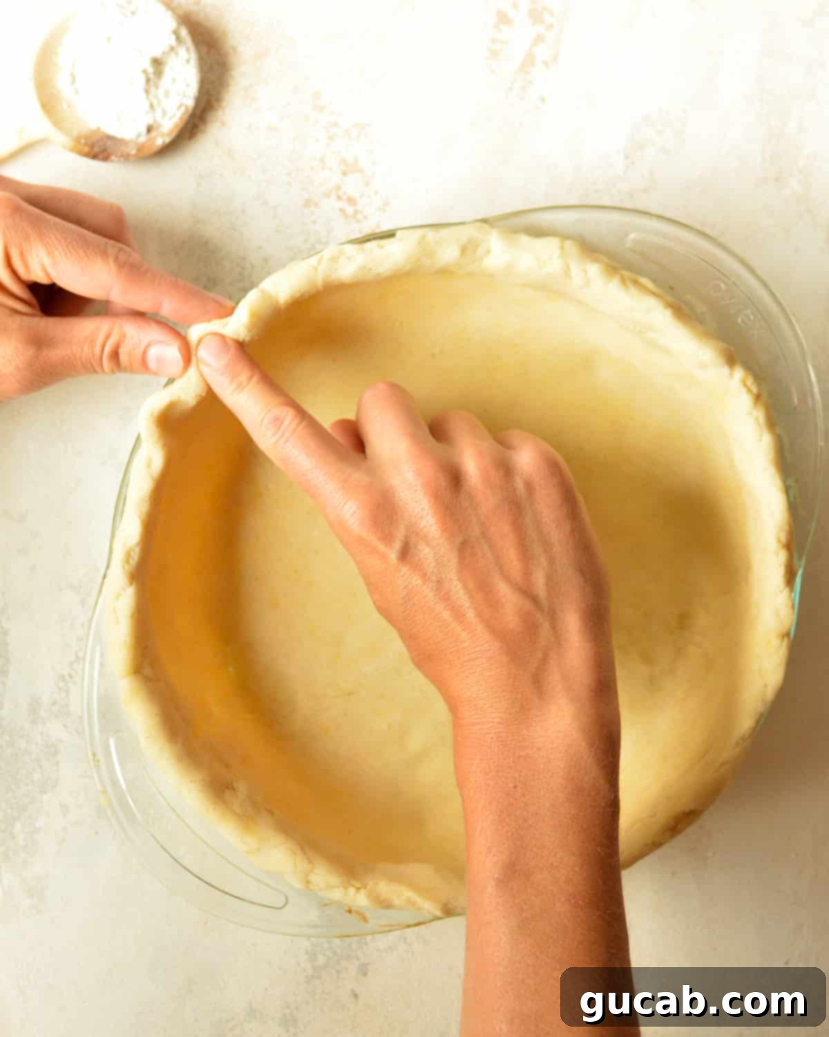 Hands demonstrating how to crimp the edges of a gluten-free pie crust.