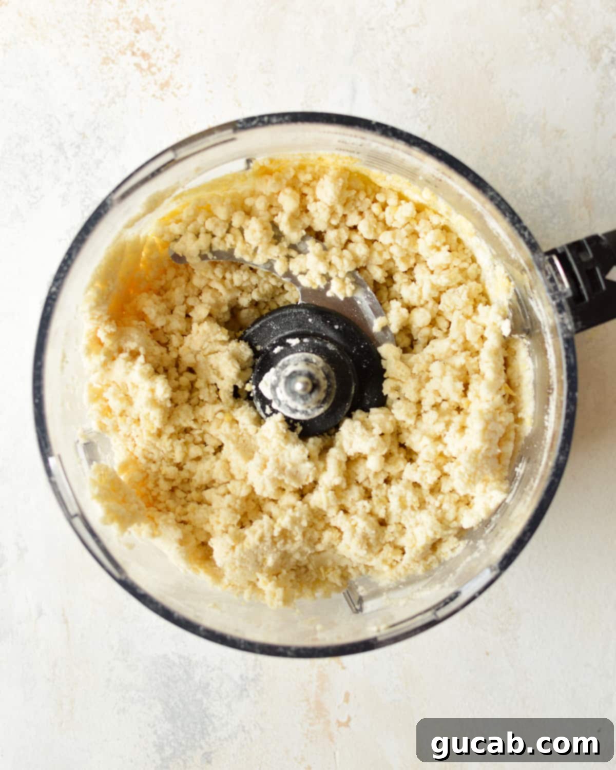 Gluten-free pie dough mixture in a food processor after adding wet ingredients, appearing thick and crumbly.