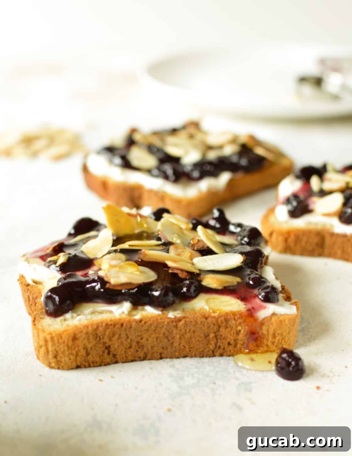 three pieces of toast with blueberry jam, cream cheese, and sliced almonds