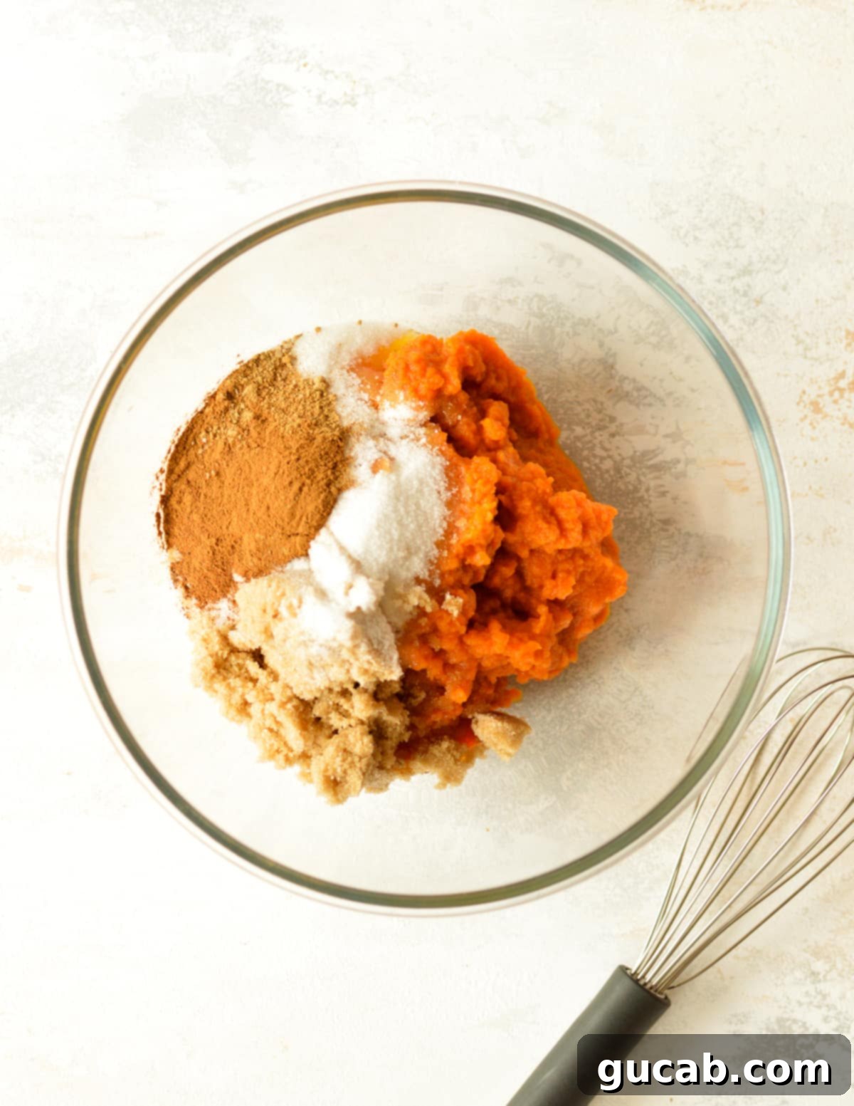 A bowl containing pumpkin puree, sugar, and various spices, ready for mixing to create the pie filling.