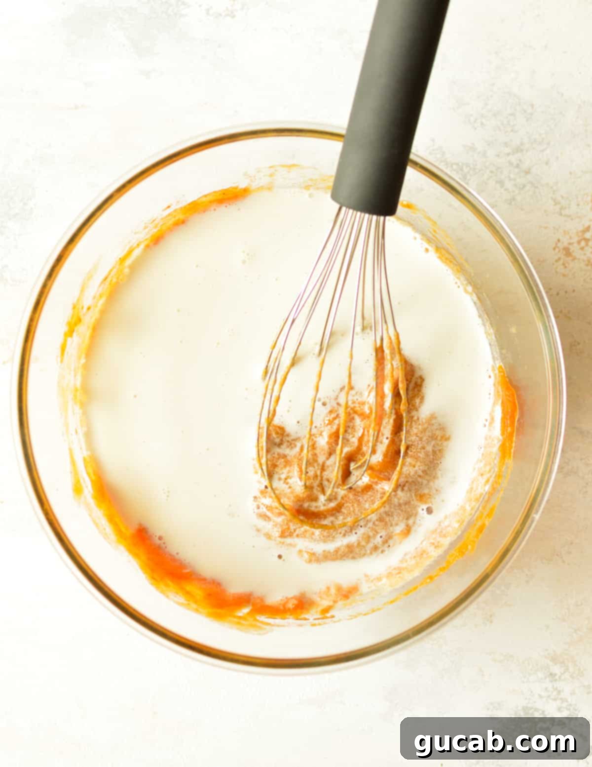 Pumpkin pie filling being mixed with half and half in a large bowl, showing its creamy texture.