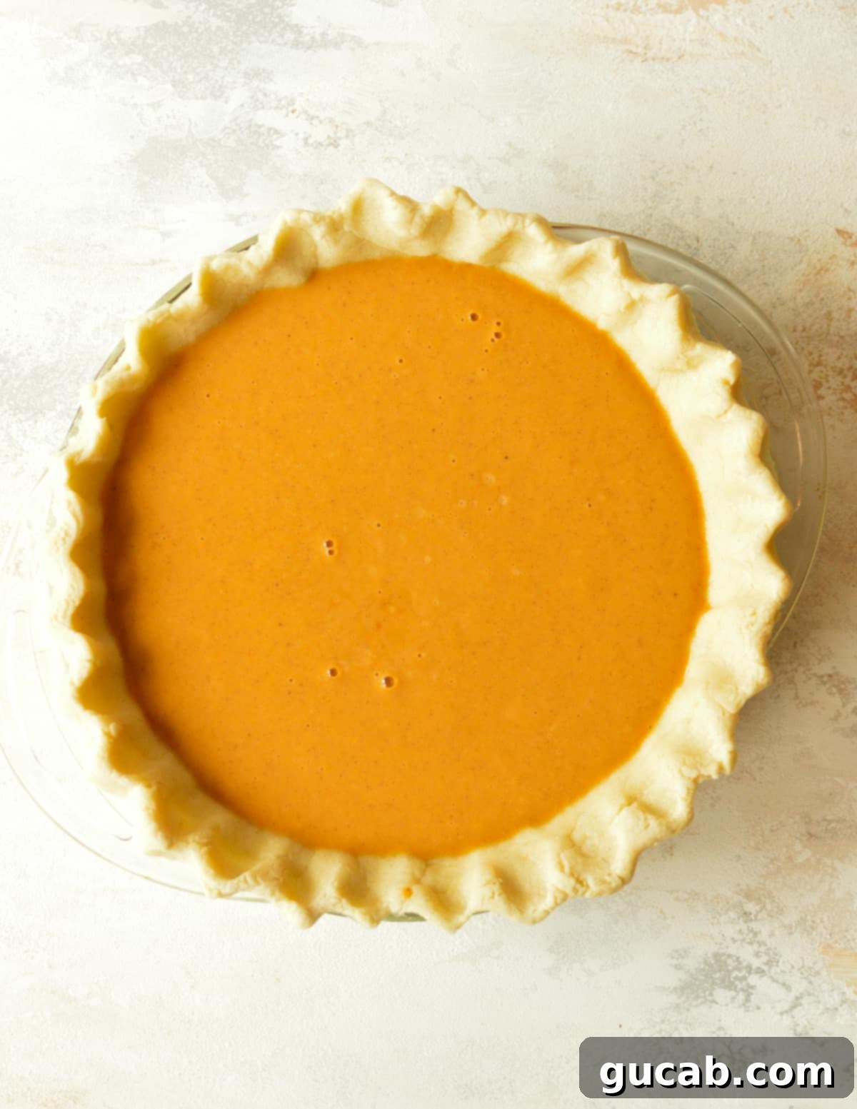 Pumpkin pie filling poured into a par-baked pie crust, ready for baking.