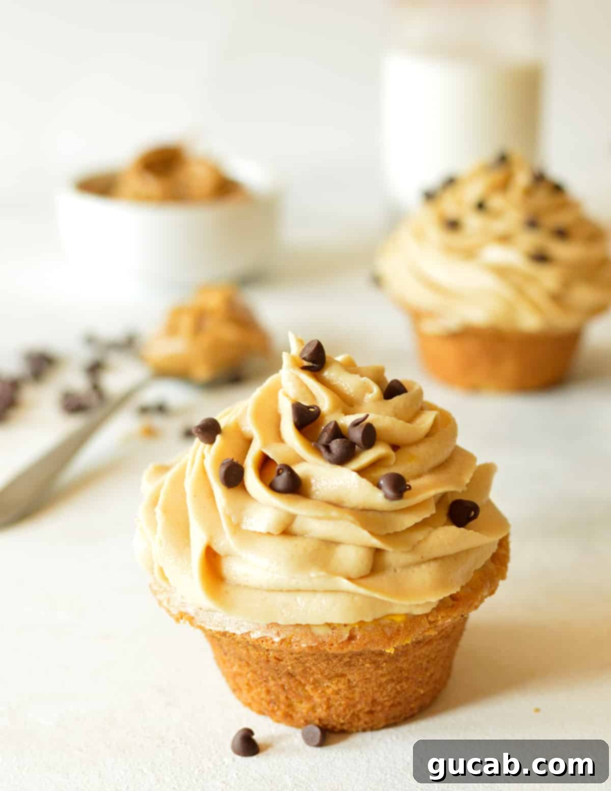 A vanilla cupcake adorned with a generous swirl of peanut butter cream cheese frosting and sprinkled with chocolate chips