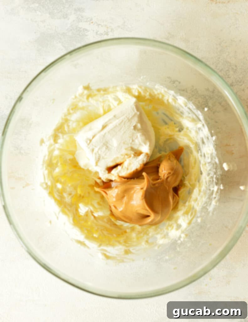 Softened cream cheese, creamy peanut butter, and vanilla extract added to the bowl with the creamed butter, ready for mixing.