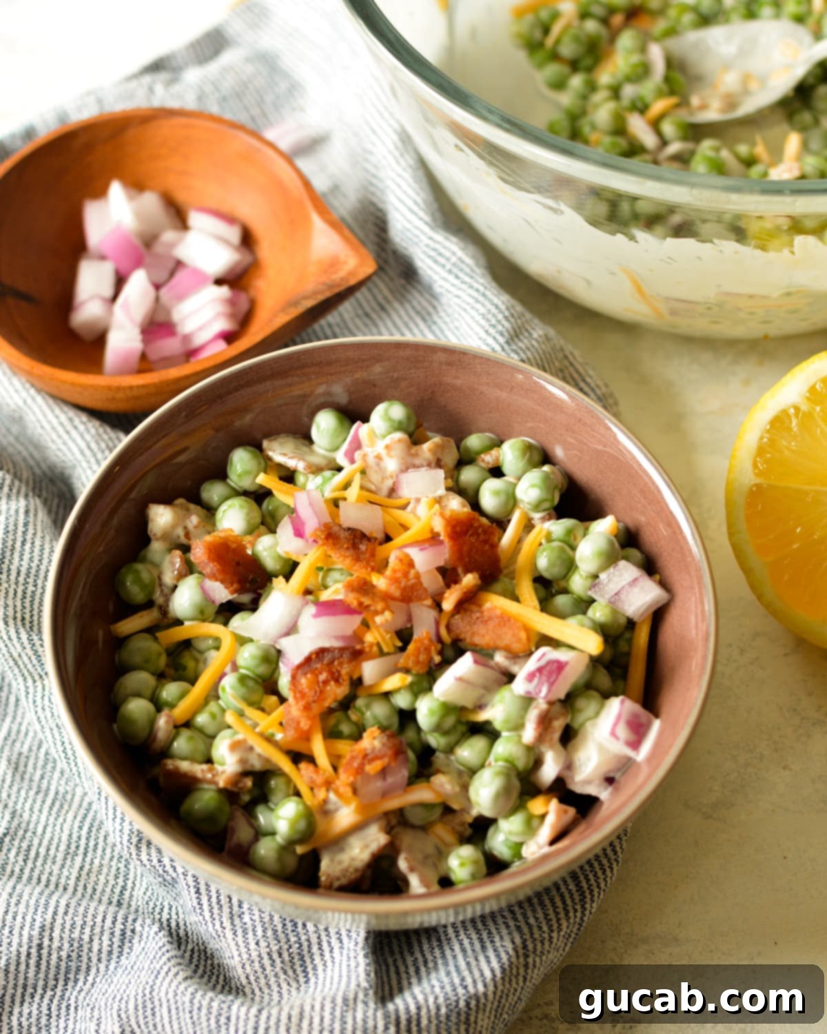 A vibrant bowl of creamy English pea salad with visible sweet peas, crispy bacon, and shredded cheddar cheese, ready to be served.