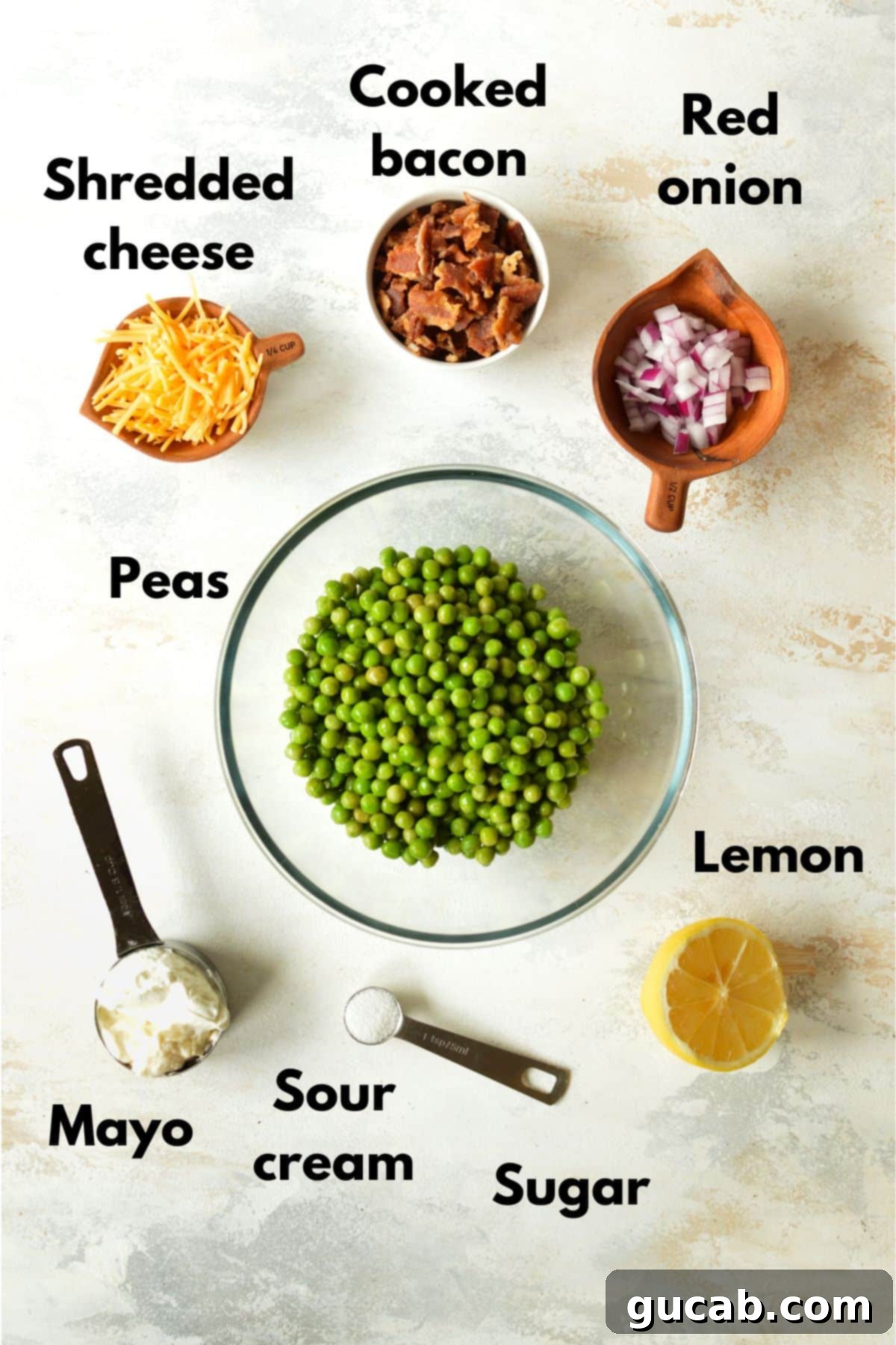 A visual display of all ingredients for English pea salad: a bag of frozen peas, shredded cheddar cheese, crispy bacon bits, diced red onion, mayonnaise, sour cream, and a small bowl of sugar.