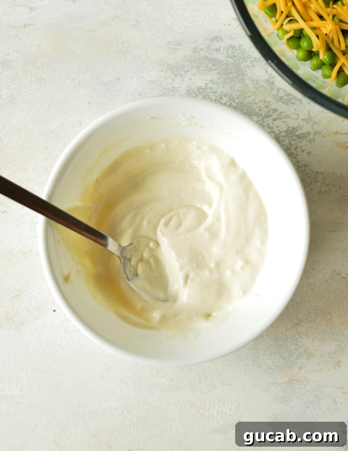 A small glass bowl containing a creamy, white mayo-based dressing, ready to be mixed into the salad.