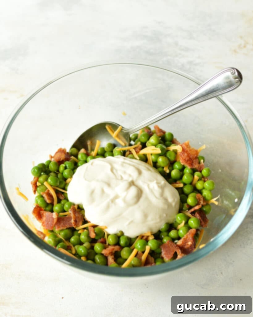 A close-up shot of the English pea salad being mixed with the creamy dressing in a large bowl, showing the vibrant colors of the ingredients.