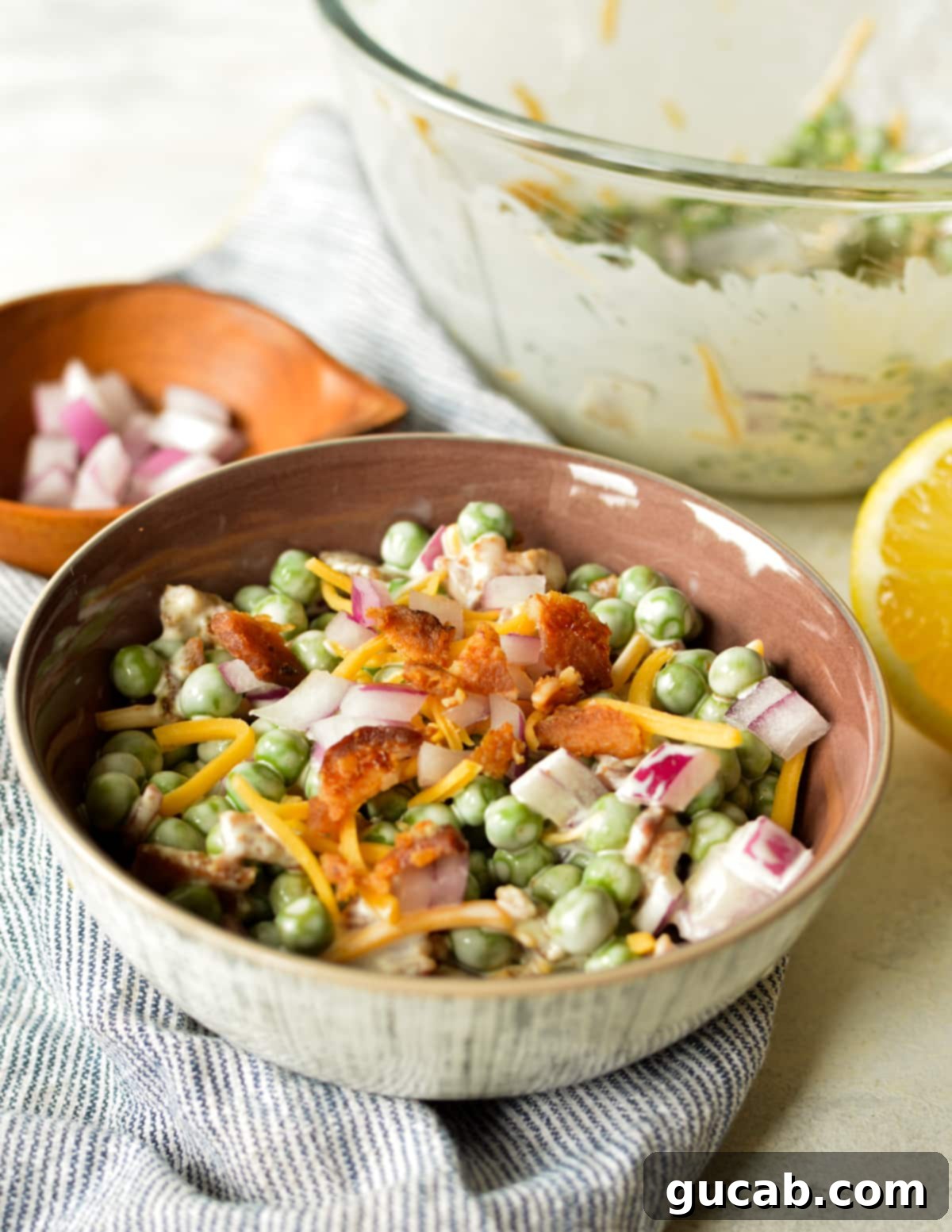 A beautifully presented bowl of English pea salad, garnished with extra crispy bacon and shredded cheese, ready to be enjoyed as a side dish.