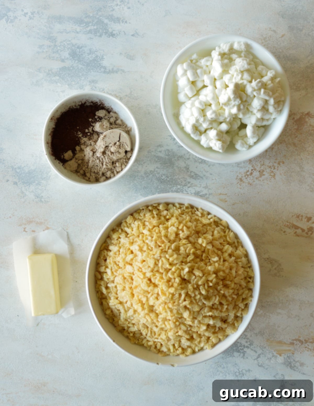 A collection of ingredients for protein rice crispy treats, including mini marshmallows, cocoa powder, chocolate protein powder, and rice cereal.