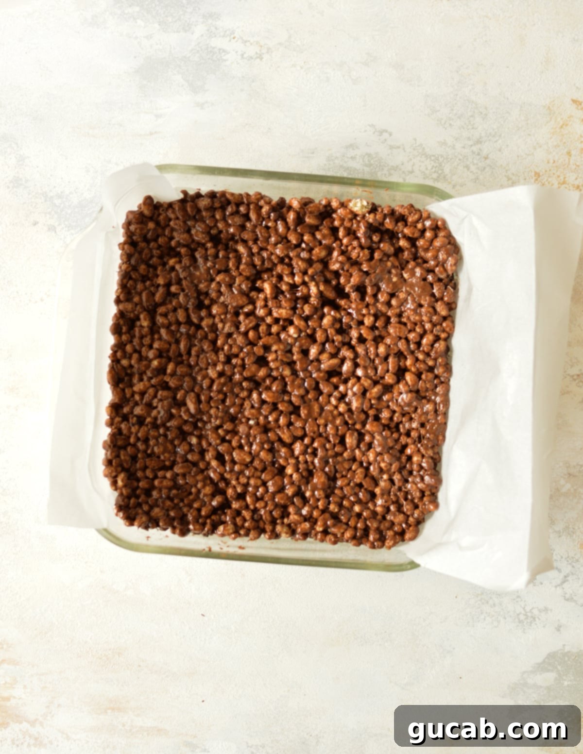 Freshly made chocolate rice krispy treats mixture being gently pressed into a parchment-lined pan.