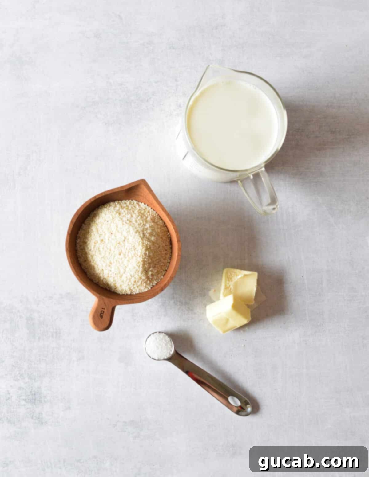 Hearty Creamy Grits 3 A simple flat lay showing the four essential ingredients for creamy grits: a glass of milk, a stick of butter, a bowl of kosher salt, and a bag of stoneground grits.