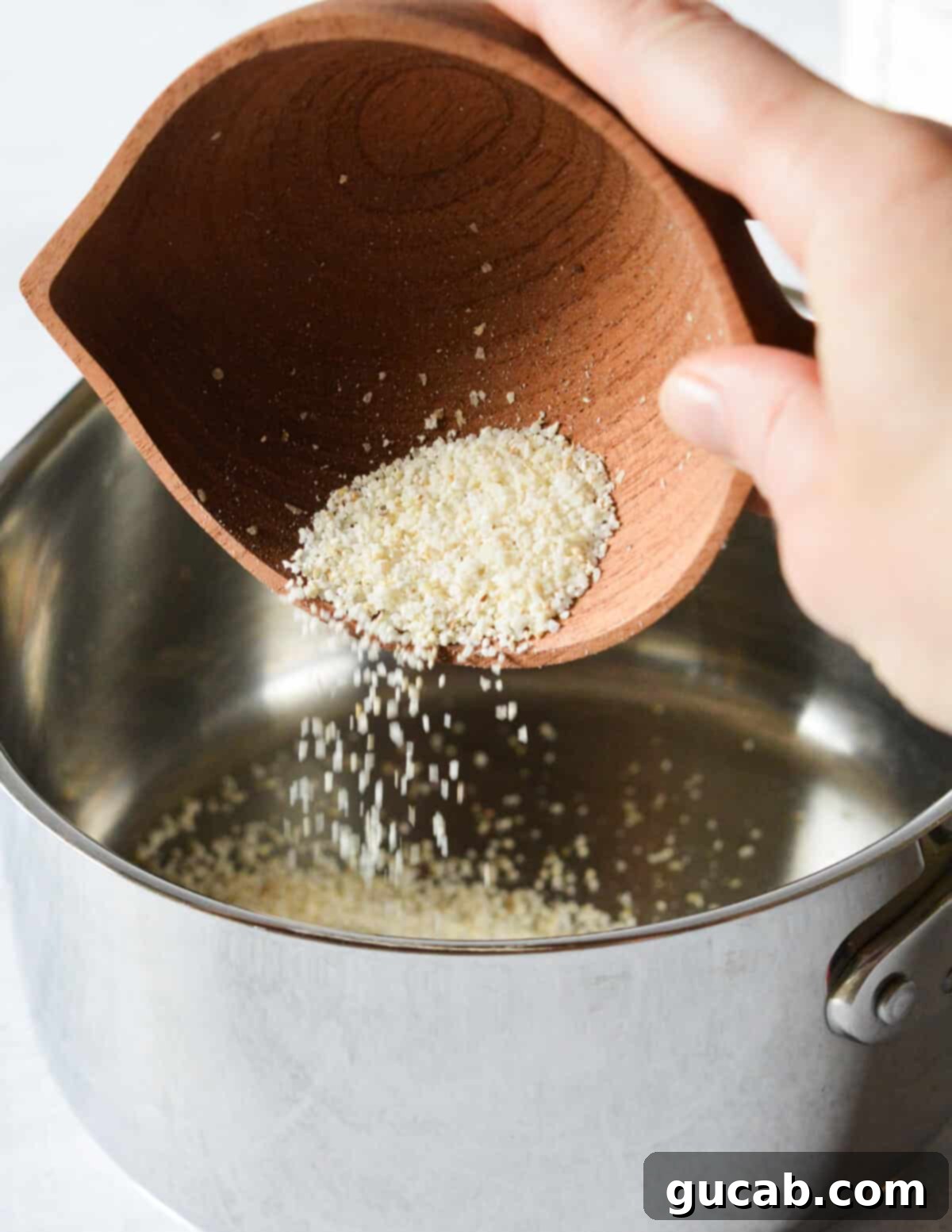 Hearty Creamy Grits 4 A hand pouring dry stoneground grits into a medium saucepan.