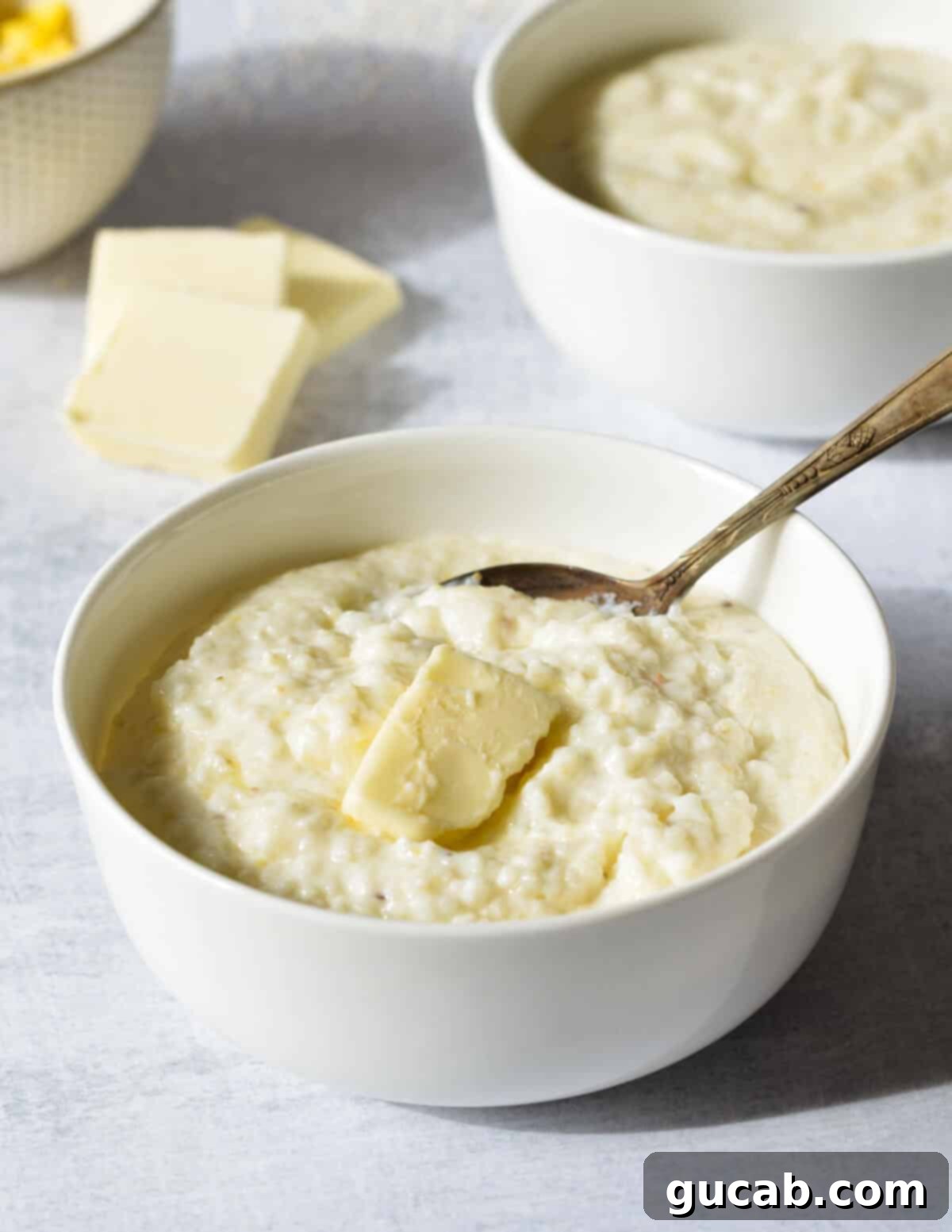 Hearty Creamy Grits 9 A warm bowl of creamy grits with a melting pat of butter, with a spoon resting in it, signifying readiness to eat.
