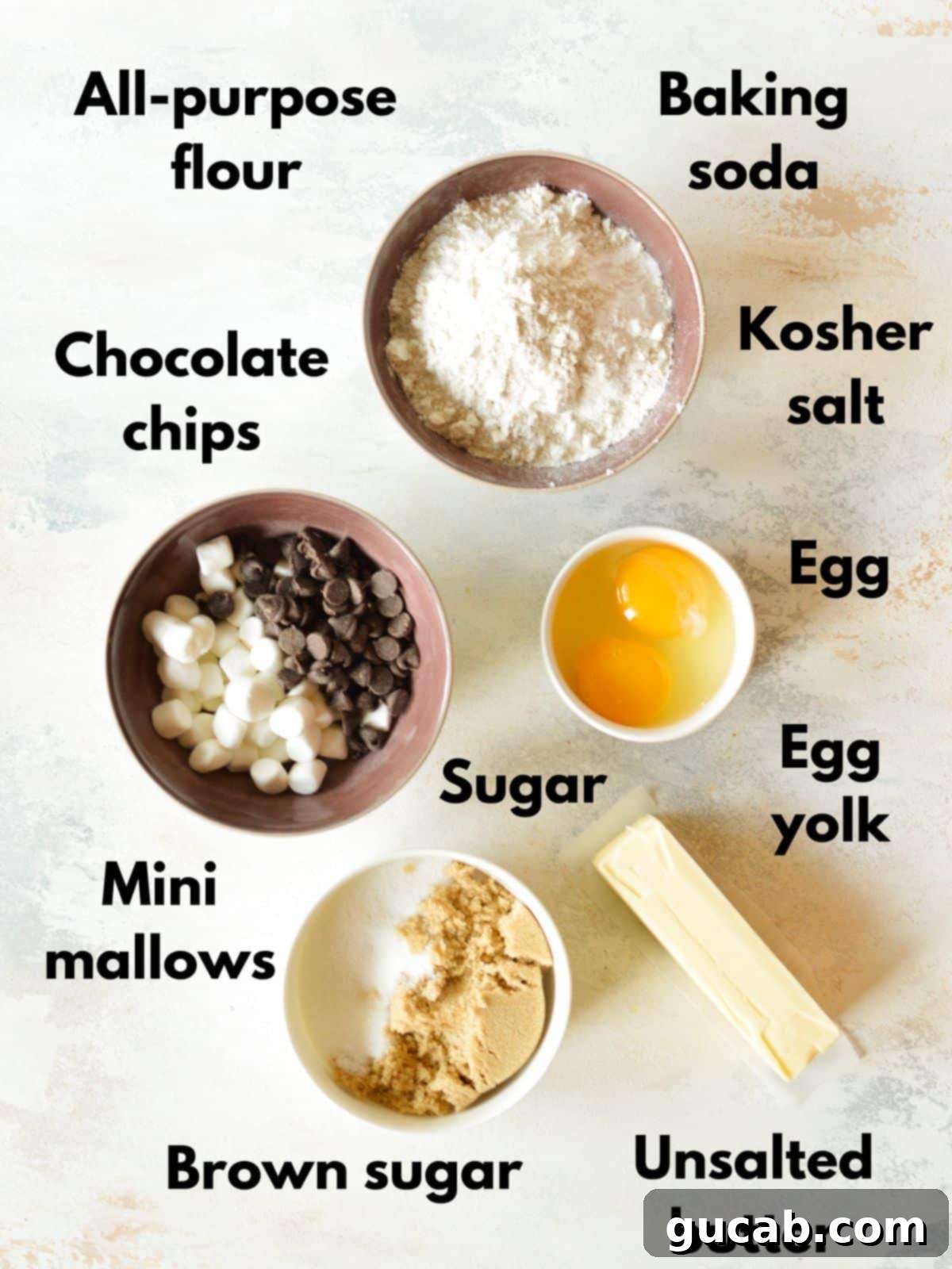 various ingredients for chocolate chip marshmallow cookies laid out on a table, including flour, sugars, butter, and marshmallows
