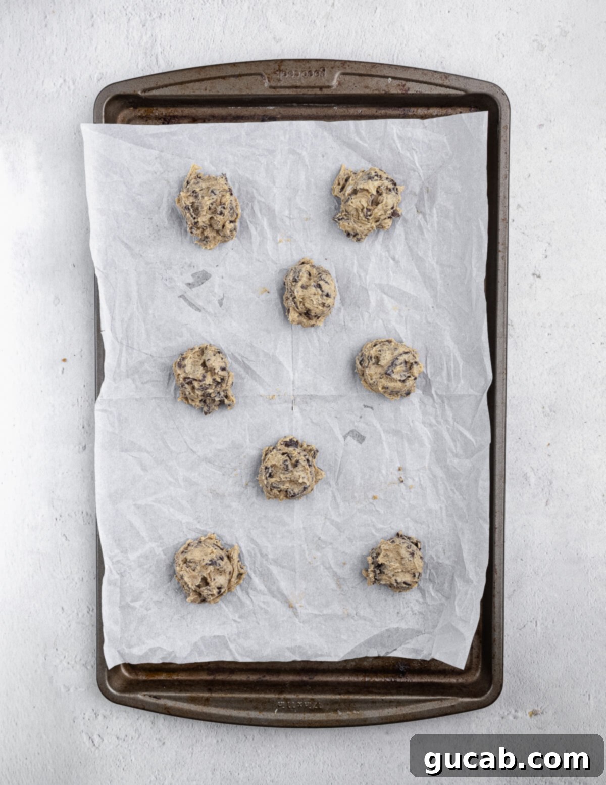 Uniform balls of chocolate chip Oreo cookie dough perfectly arranged on a parchment-lined baking sheet, ready for the oven.