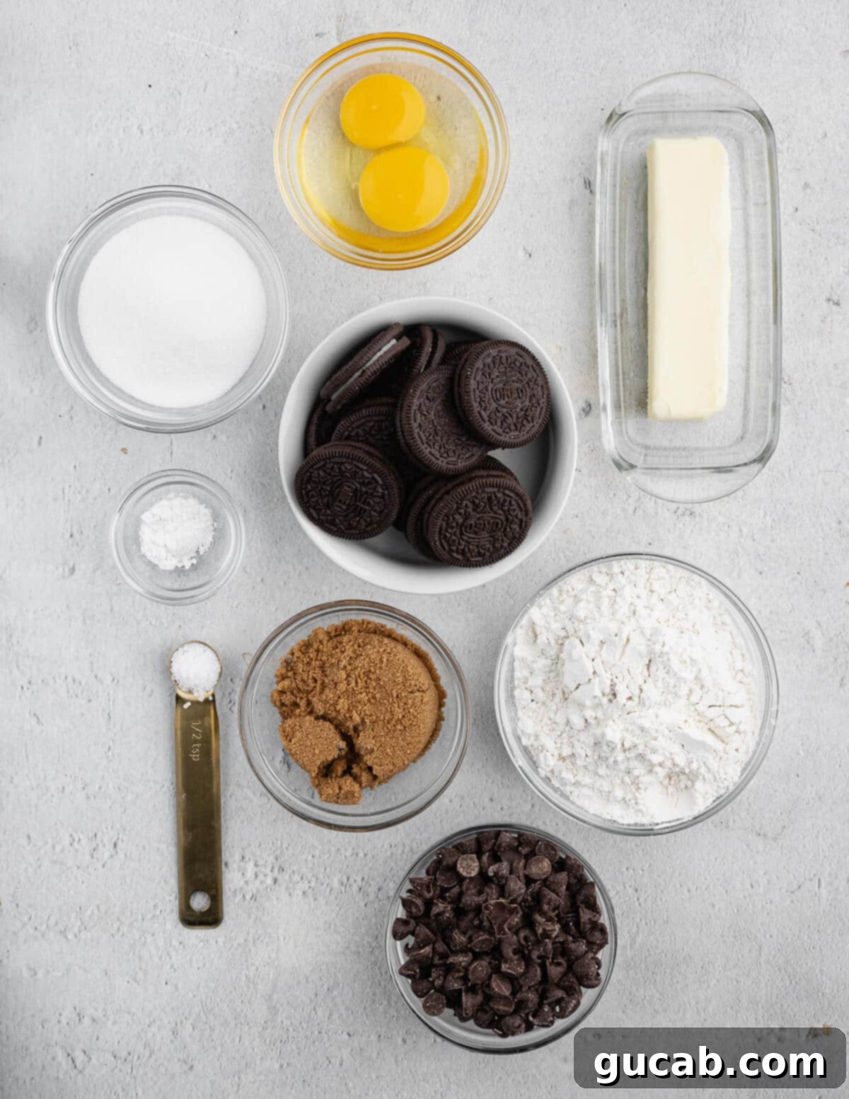 A top-down view of all the essential ingredients laid out for baking Oreo chocolate chip cookies: fresh eggs, softened butter, iconic Oreos, granulated sugar, all-purpose flour, rich chocolate chips, brown sugar, baking powder, and a pinch of salt.