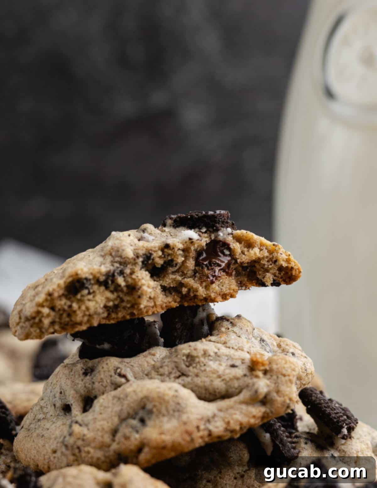 A stack of golden-brown Oreo chocolate chip cookies with a bite taken out of the top one, revealing its soft, chewy interior filled with chocolate and Oreo chunks.