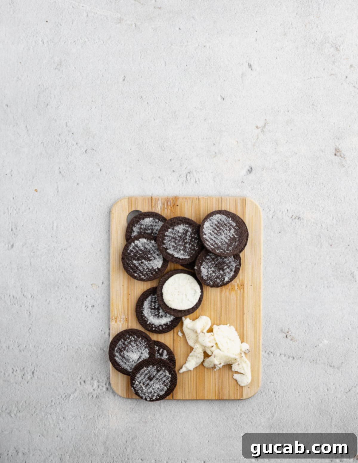 Five Oreo cookies laid out on a cutting board, with the cream filling removed from each, ready to be crushed into crumbs.