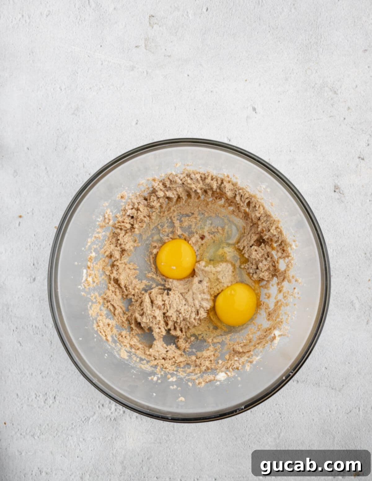 The creamed butter and sugar mixture in a bowl, with a cracked egg and a separated egg yolk resting on top, ready to be beaten in.