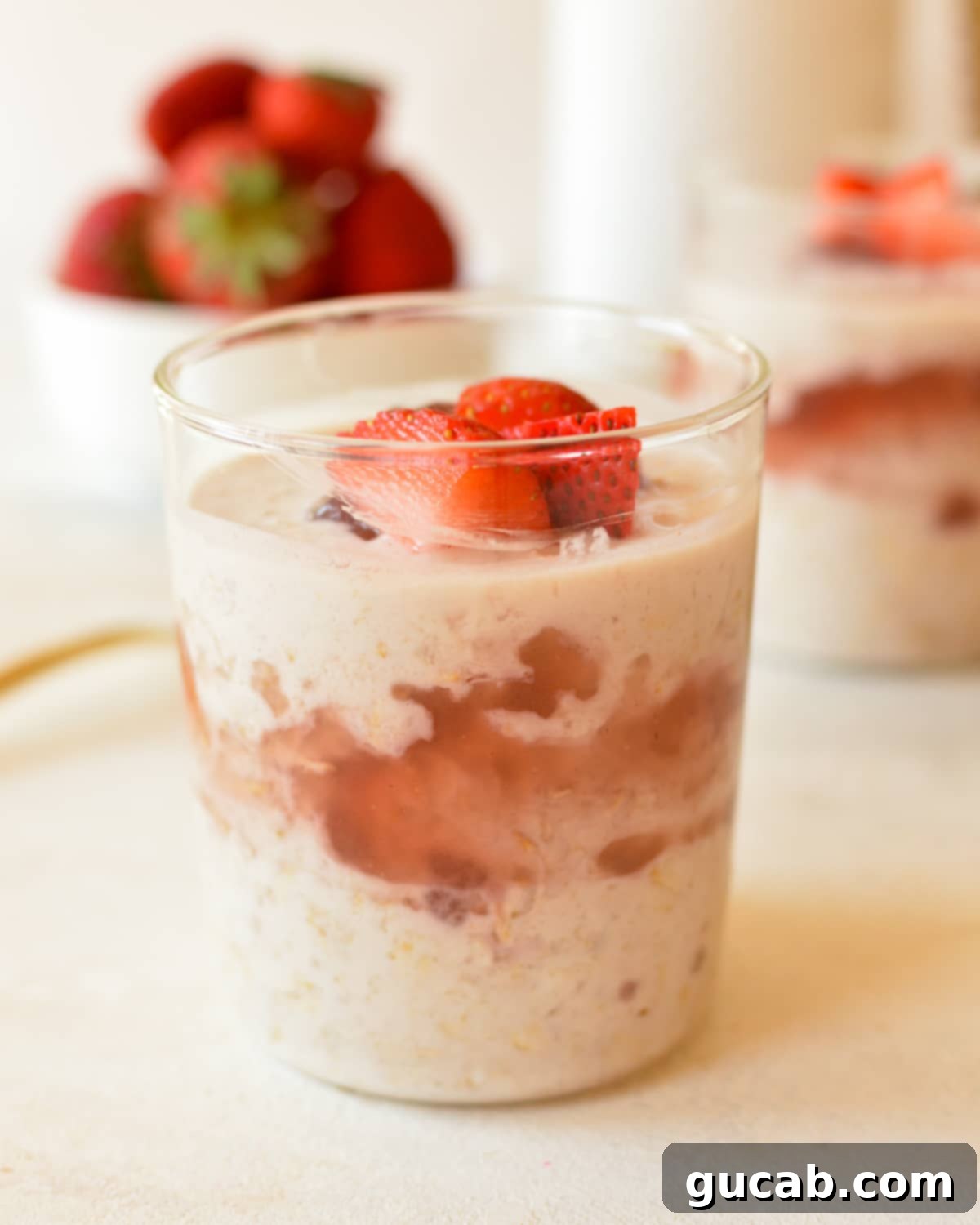A glass of creamy overnight oats layered with jam and fresh strawberries, ready to be enjoyed as a healthy and quick breakfast.