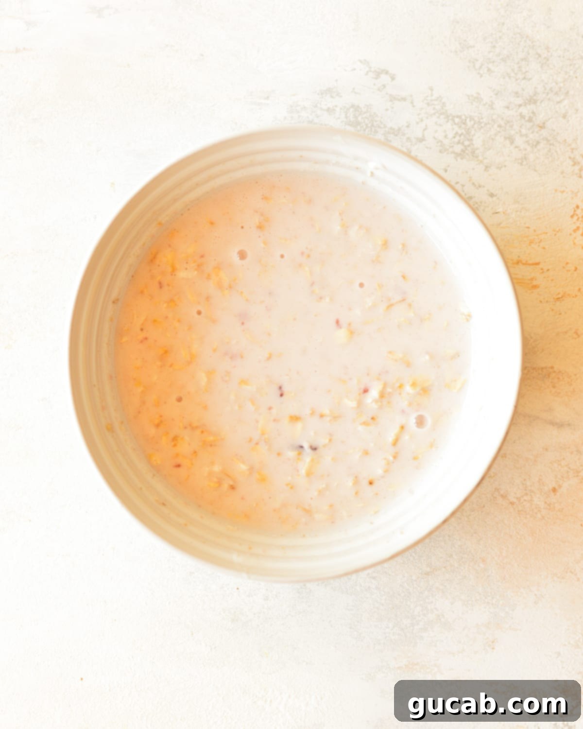 A bowl of overnight oats mixture, stirred thoroughly with water, jam, and yogurt, showing a smooth and uniform consistency.
