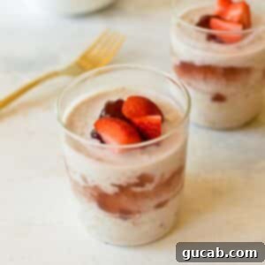Two glasses of creamy raspberry overnight oats with fresh strawberries on top, ready for a delicious breakfast.