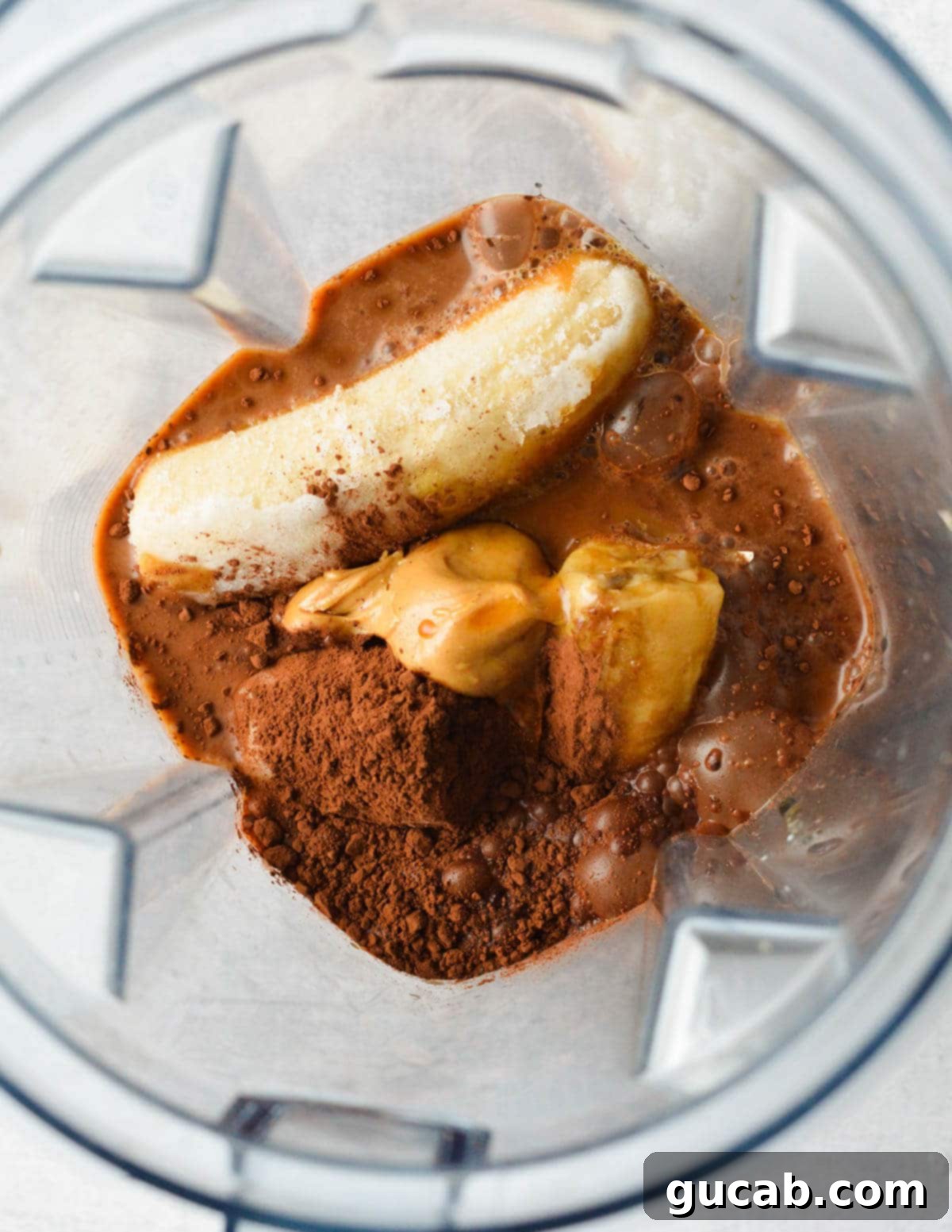 a blender with banana, peanut butter, coffee, cocoa powder, and milk in it. 