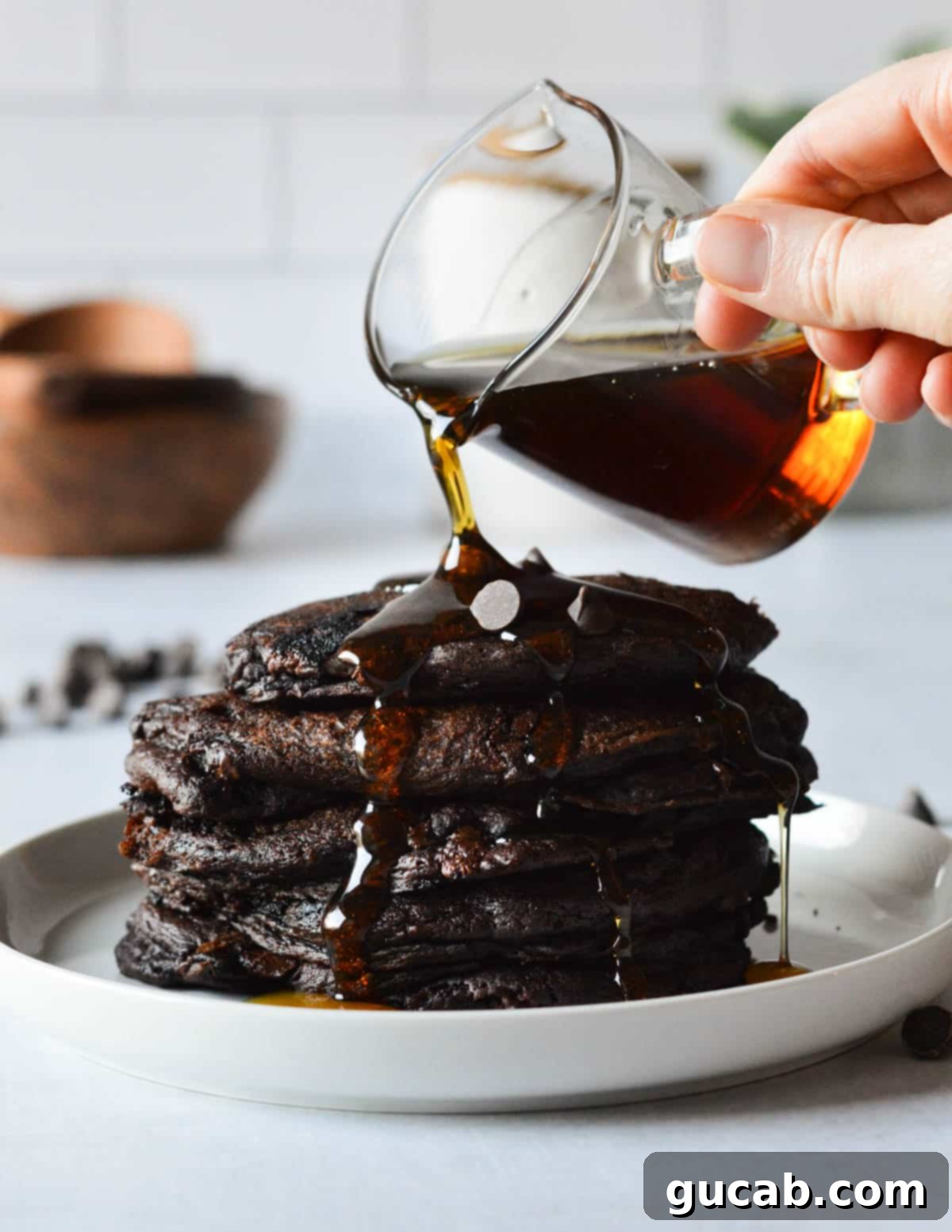 Guilt-Free Chocolate Pancake Indulgence 2 Pouring maple syrup onto a stack of dark chocolate pancakes, highlighting their rich color and fluffy texture.