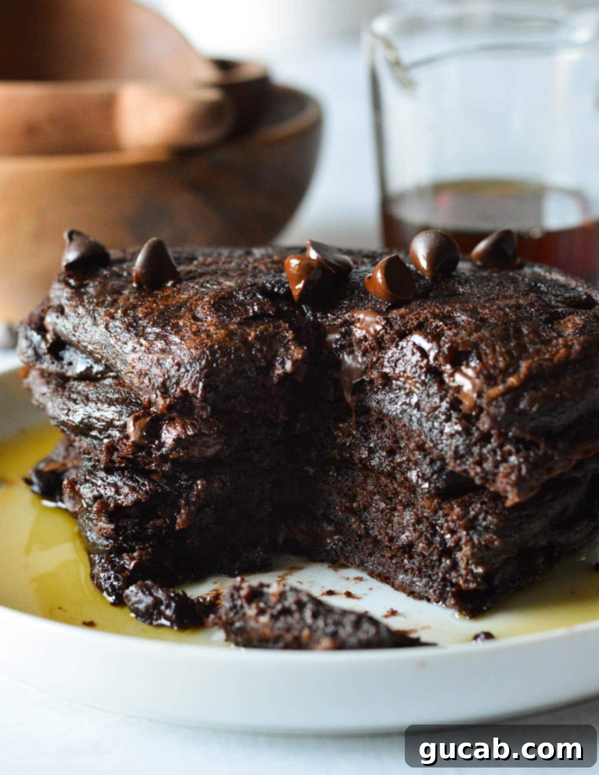 Guilt-Free Chocolate Pancake Indulgence 4 A stacked plate of dark chocolate pancakes, generously adorned with chocolate chips and a pour of syrup.