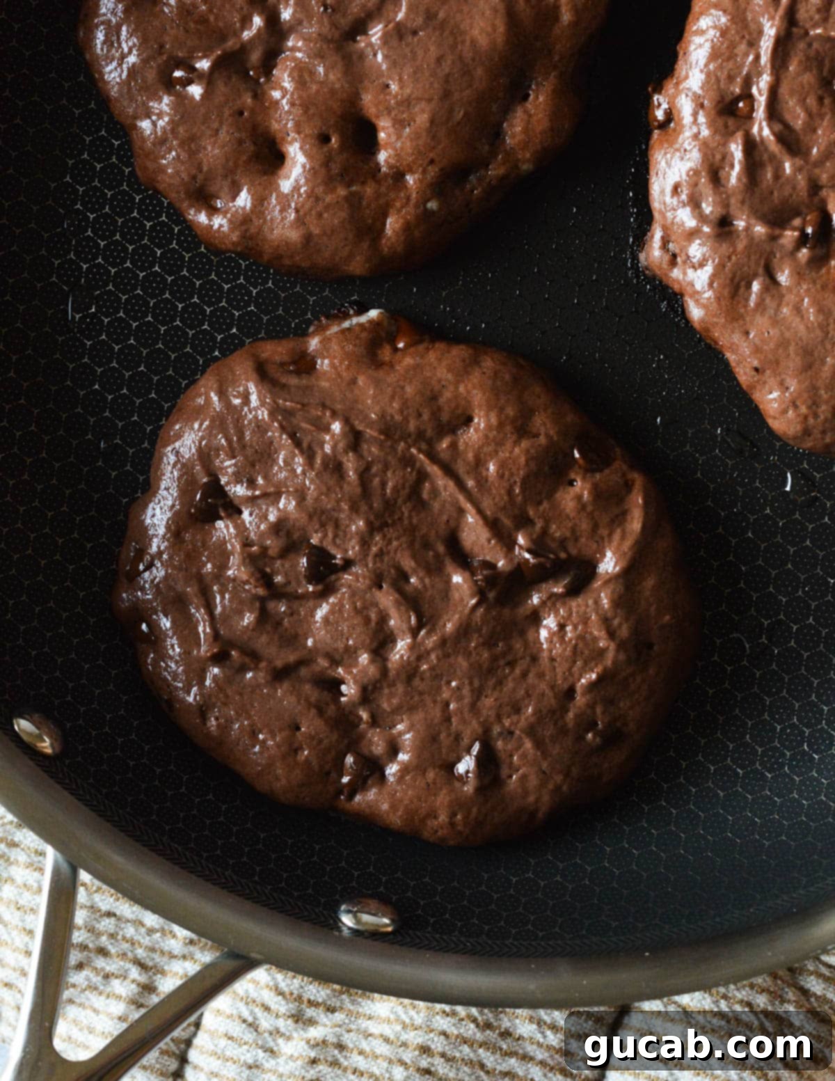 Guilt-Free Chocolate Pancake Indulgence 10 Gluten-free chocolate pancake batter cooking in a skillet, showing the beginning of the cooking process with forming bubbles.