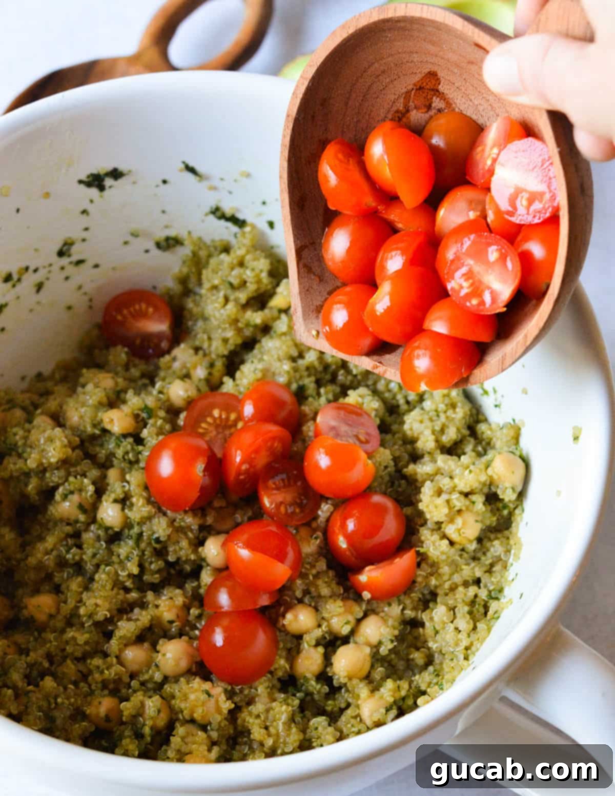 Vibrant Herb & Quinoa Power Bowl 10 dumping cherry tomatoes onto quinoa salad with chickpeas.