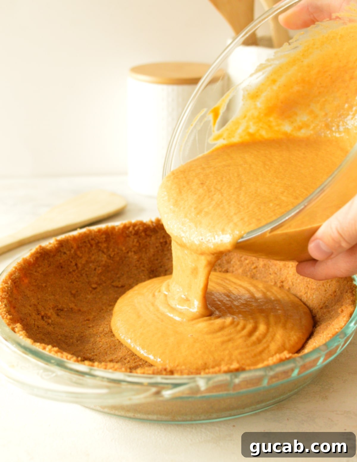 hands pouring pumpkin pie batter into crust