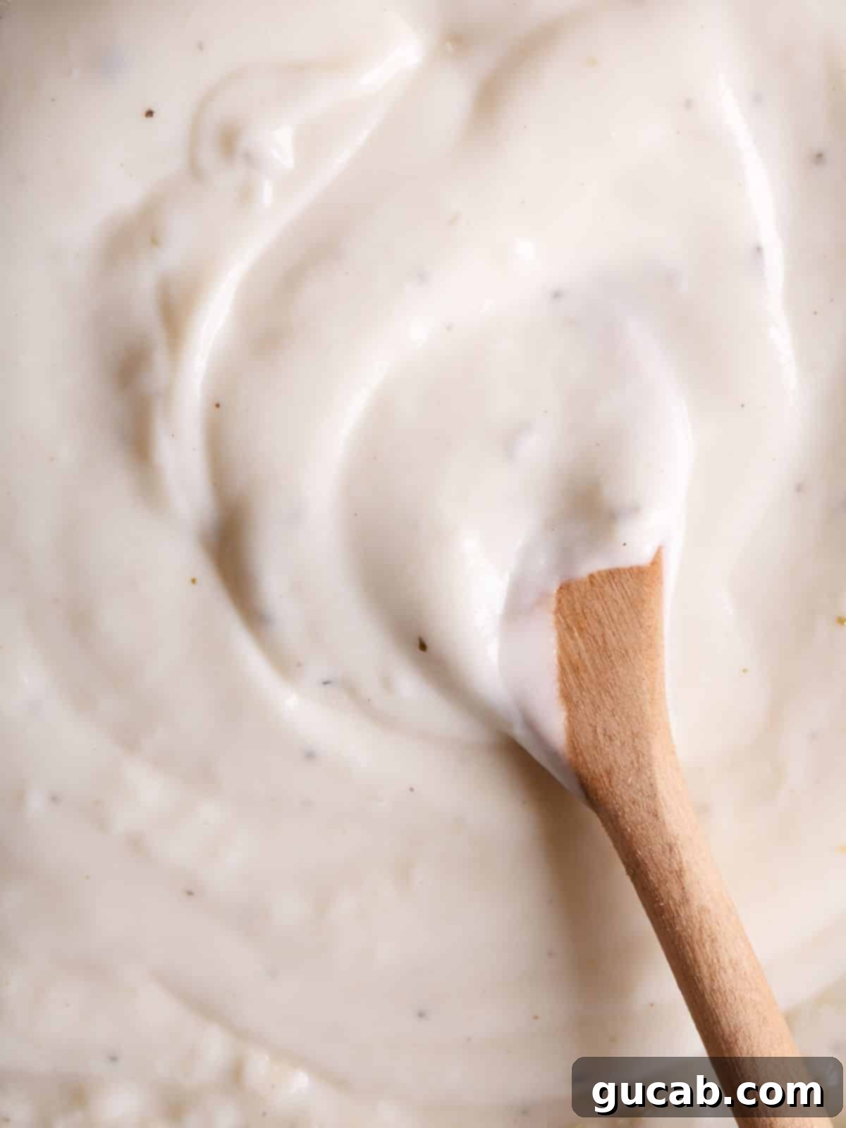 a wooden spoon stirring creamy gluten-free bechamel sauce in a saucepan