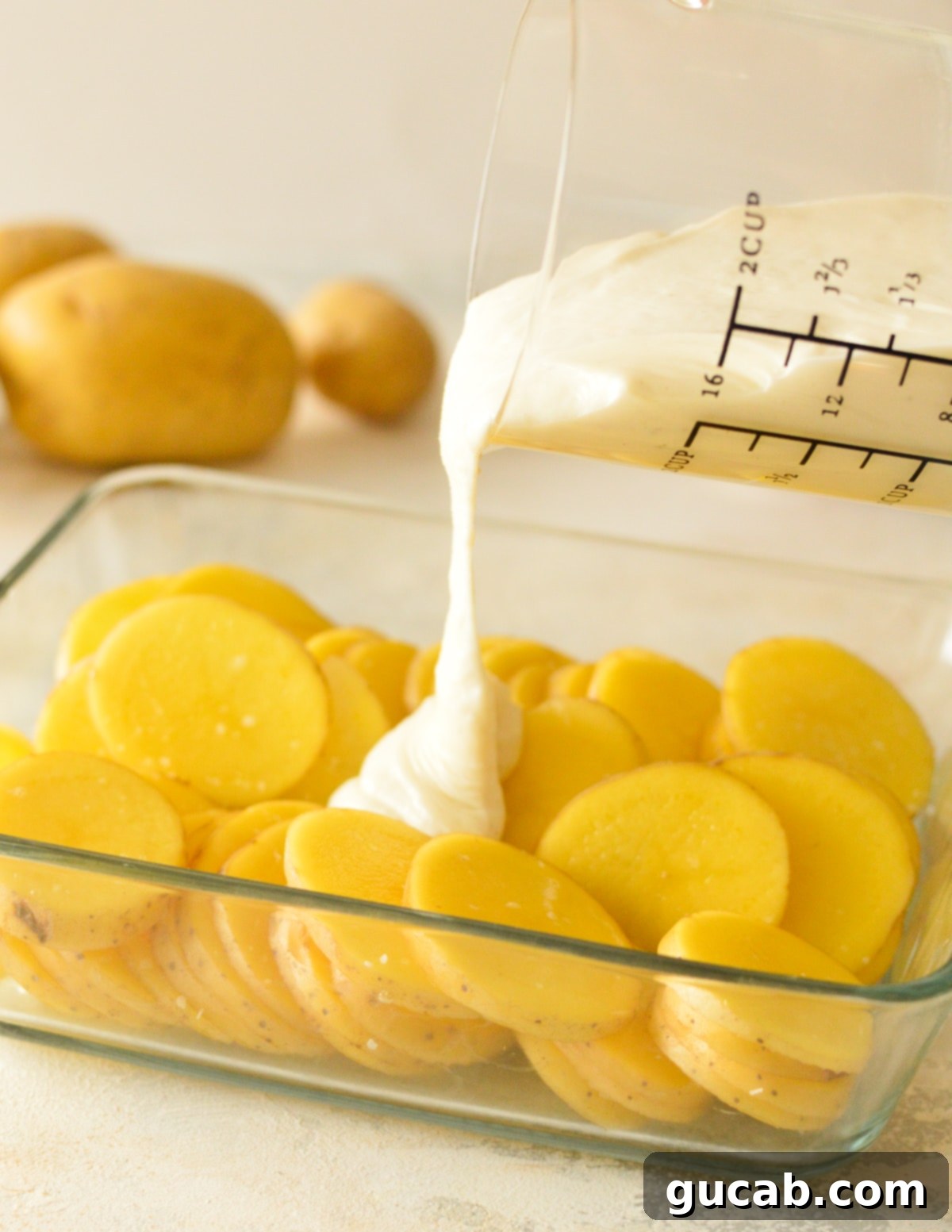 pouring gluten-free bechamel sauce over roasted potatoes