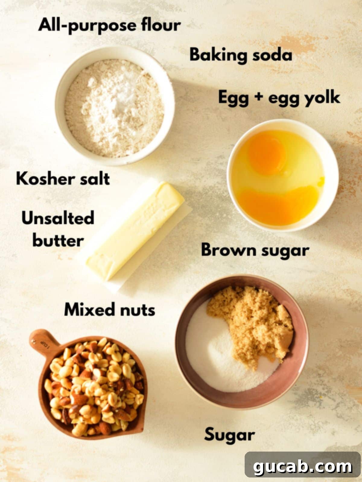 A collection of fresh ingredients laid out on a clean surface, including room-temperature butter, granulated sugar, brown sugar, eggs, all-purpose flour, baking soda, kosher salt, and a bowl of chopped mixed nuts, all ready for baking delicious cookies.