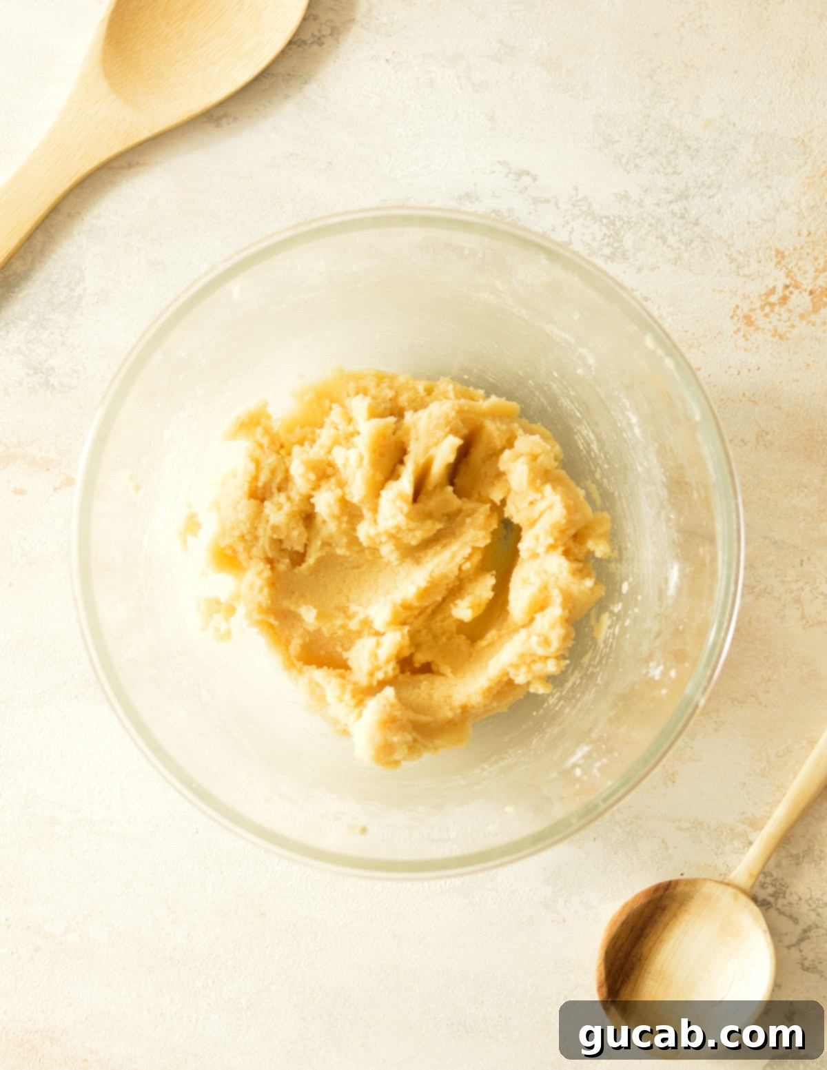 Close-up of butter and sugars being creamed together in a mixing bowl until light and fluffy, an essential step for chewy cookies.