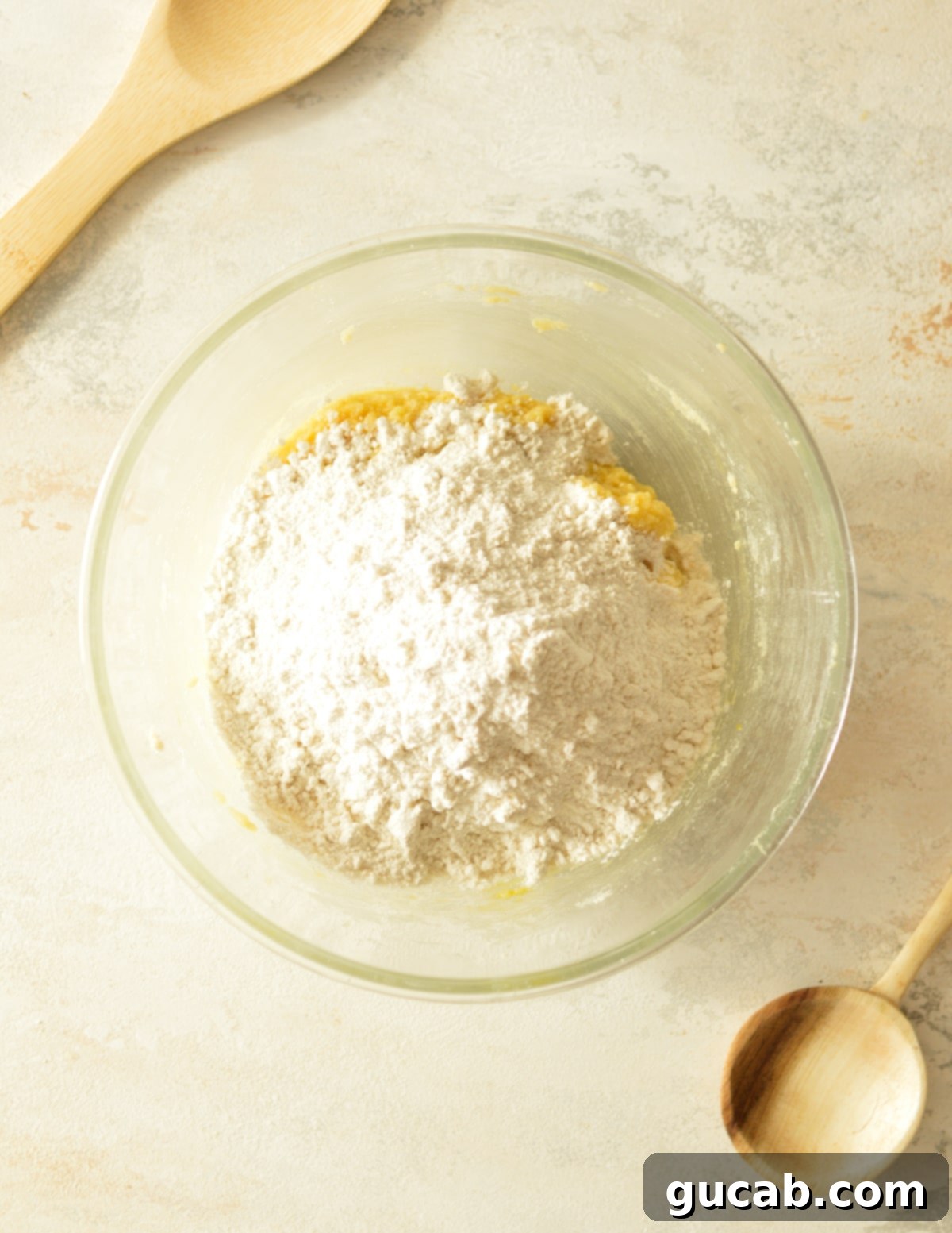 All-purpose flour, baking soda, and kosher salt precisely measured and added on top of the wet ingredients in a mixing bowl, prior to being gently combined into mixed nut cookie dough.