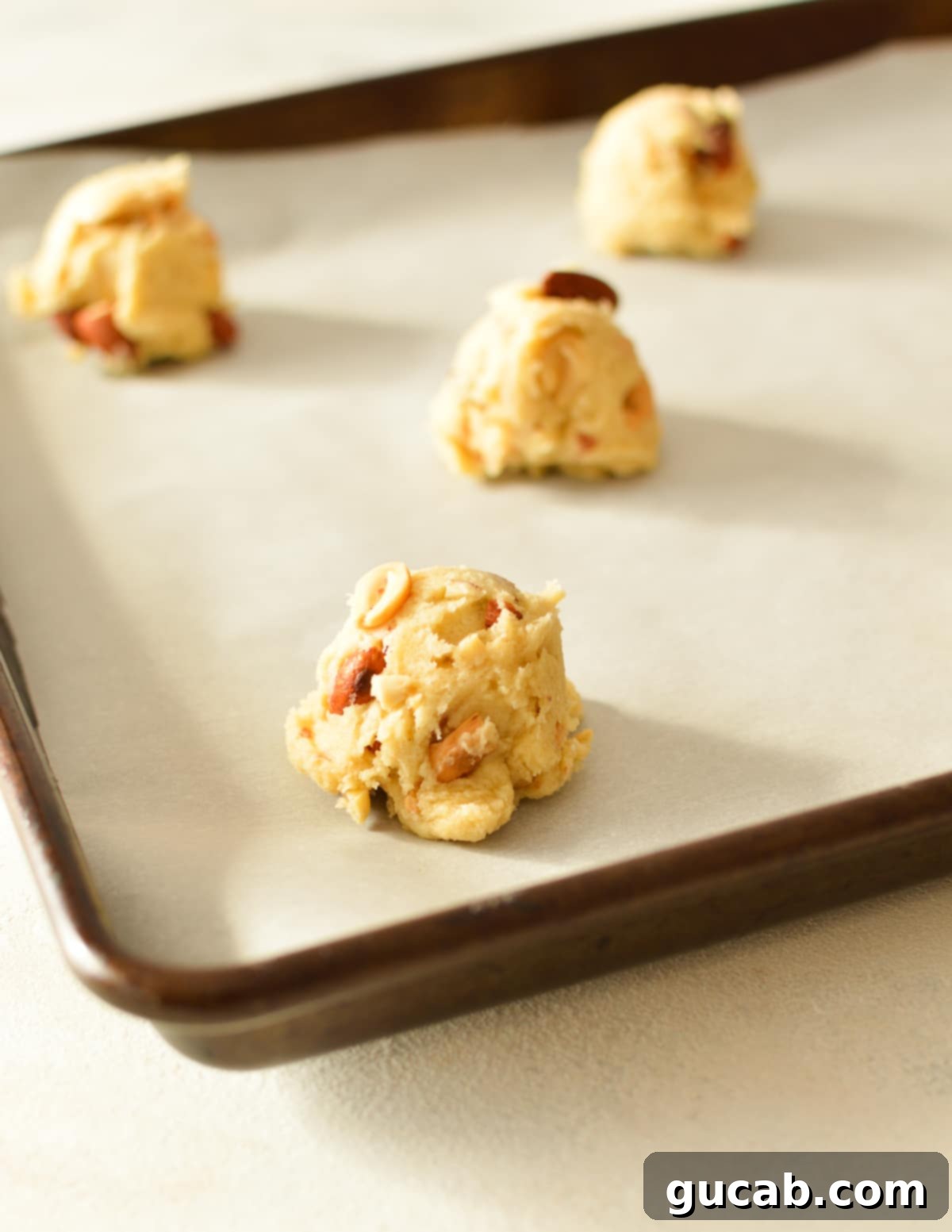 Precisely scooped portions of mixed nut cookie dough arranged on a parchment-lined baking sheet, spaced evenly and ready for the oven to create perfect cookies.