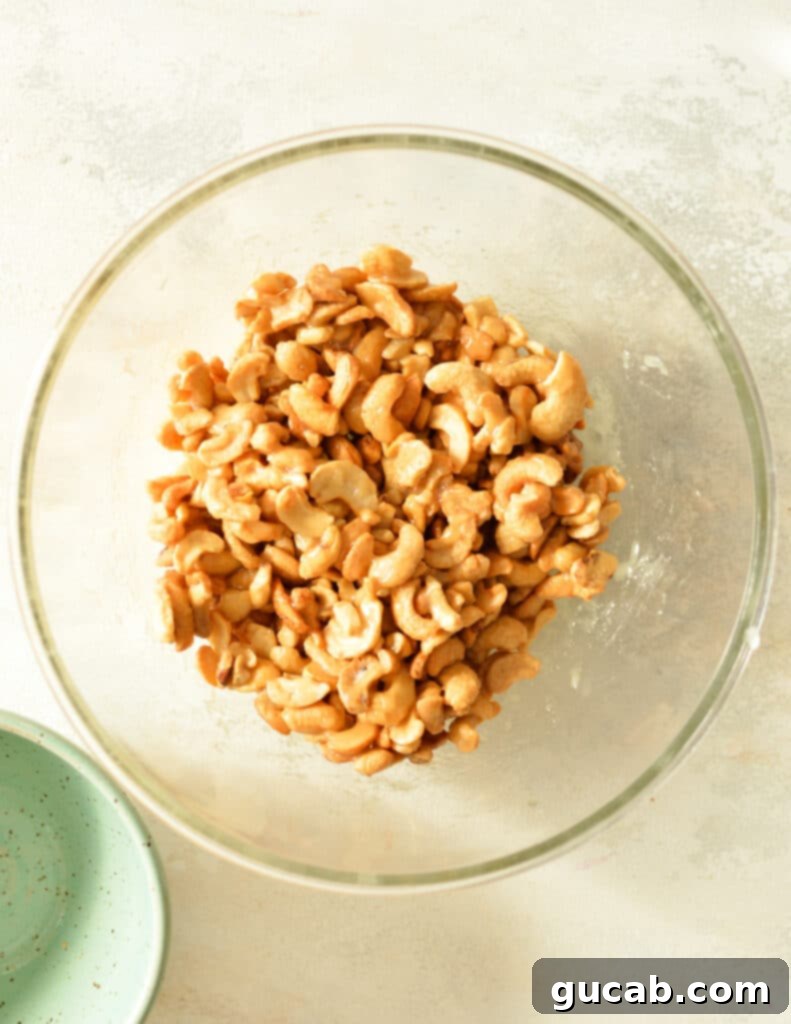 Cashews being stirred in a bowl to ensure they are fully coated with the honey-sugar mixture.