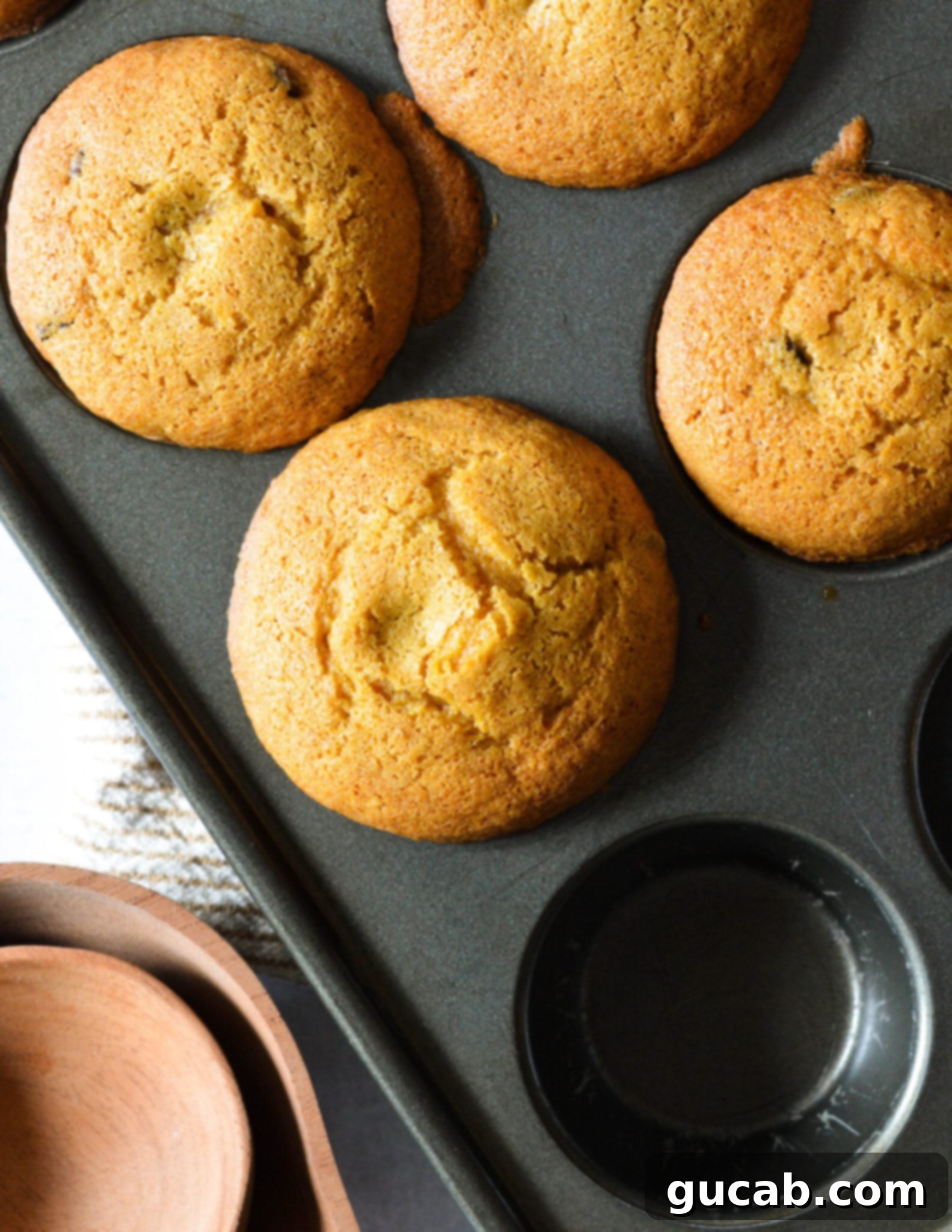 A close-up view of the golden-brown top of a freshly baked gluten-free pumpkin muffin, speckled with melted chocolate chips, hinting at its soft texture.