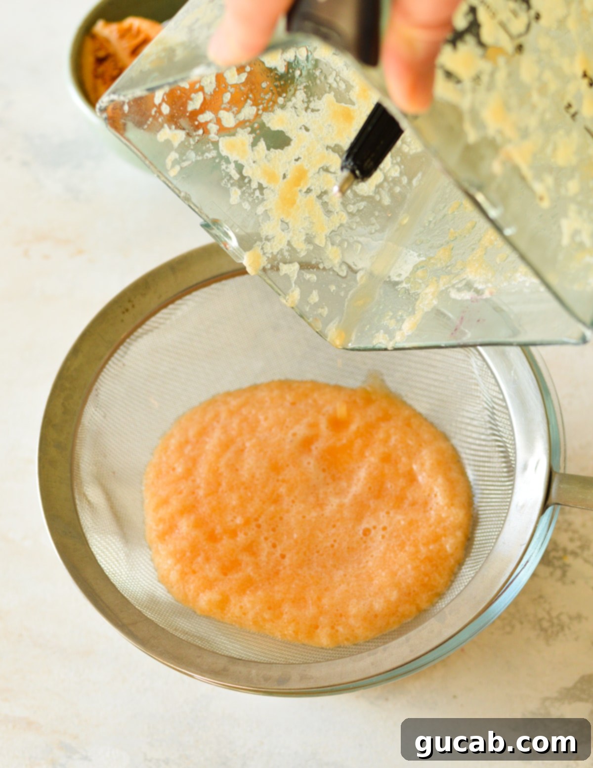 Cantaloupe puree being poured into a fine mesh sieve placed over a bowl.