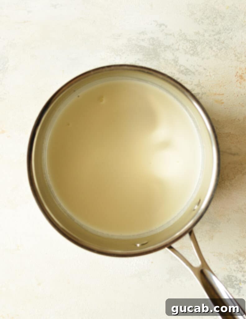 A small saucepan of heavy cream beginning to foam and boil, indicating it's ready to be poured over the chocolate and peanut butter.
