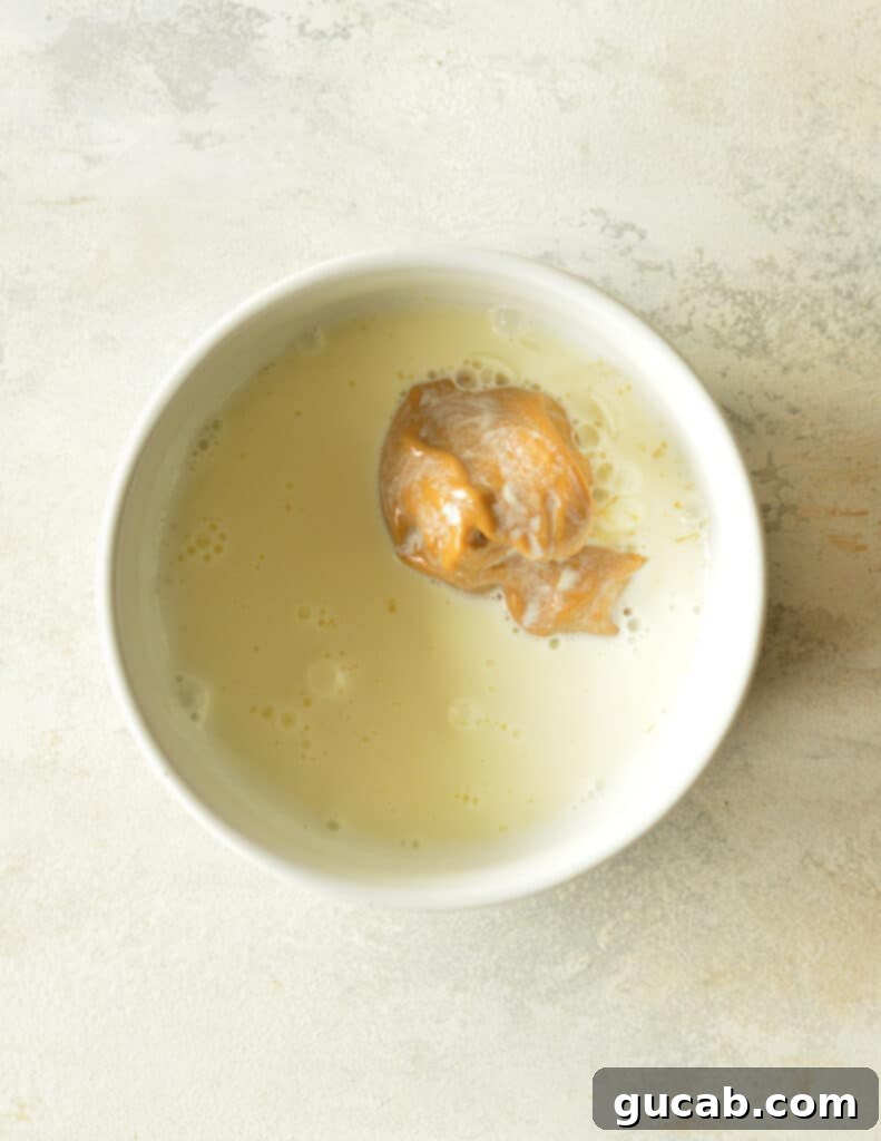 A bowl of peanut butter and white chocolate with hot cream just poured over it, before stirring, illustrating the resting phase.