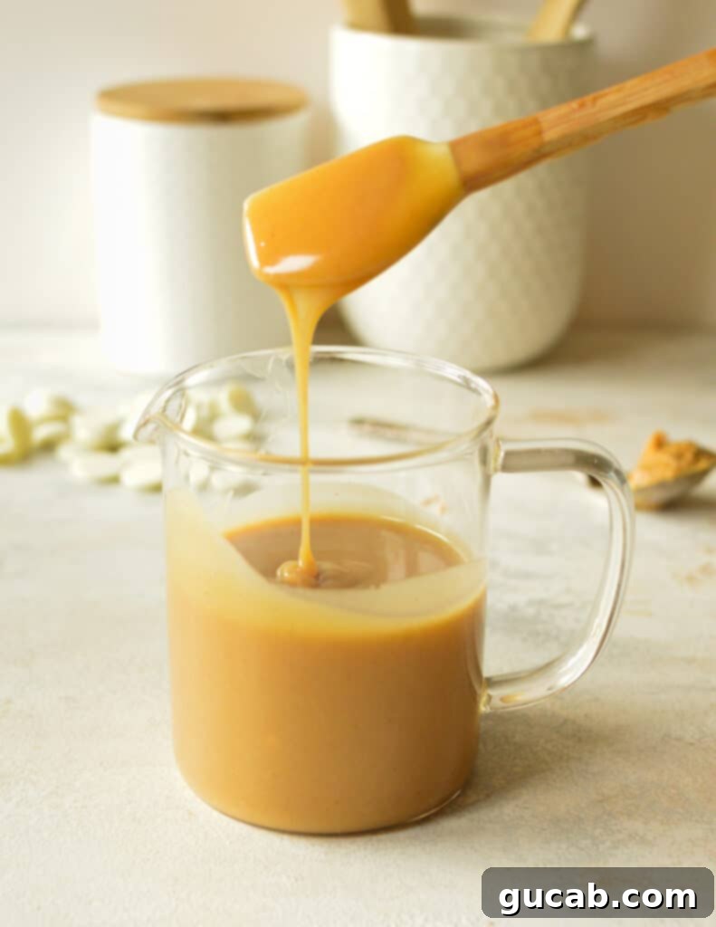 Peanut butter ganache in a bowl, with a spatula lifting some, showing its smooth and pourable consistency after 10 minutes.