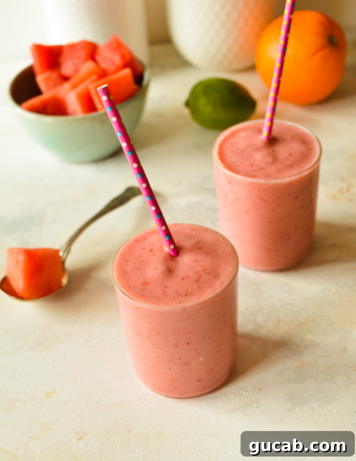 Two glasses of vibrant watermelon banana smoothies, garnished with fresh fruit and ready to drink.