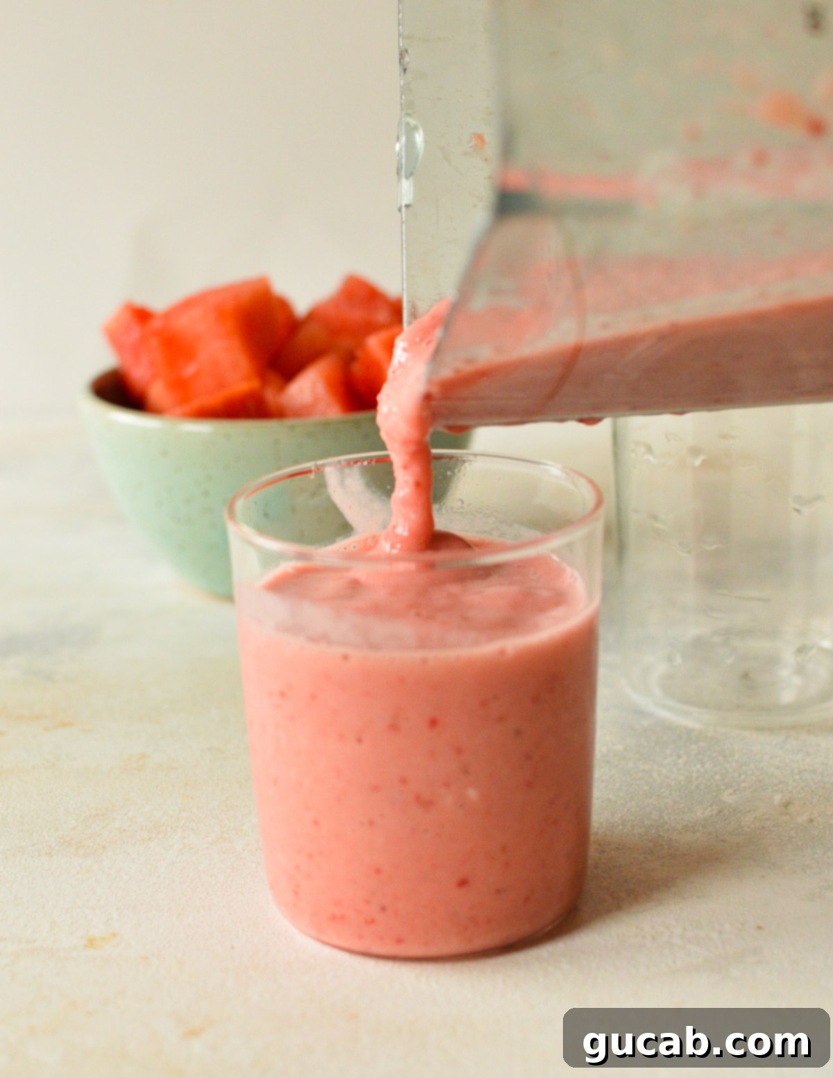 A vibrant watermelon banana smoothie being poured from a blender into a glass.