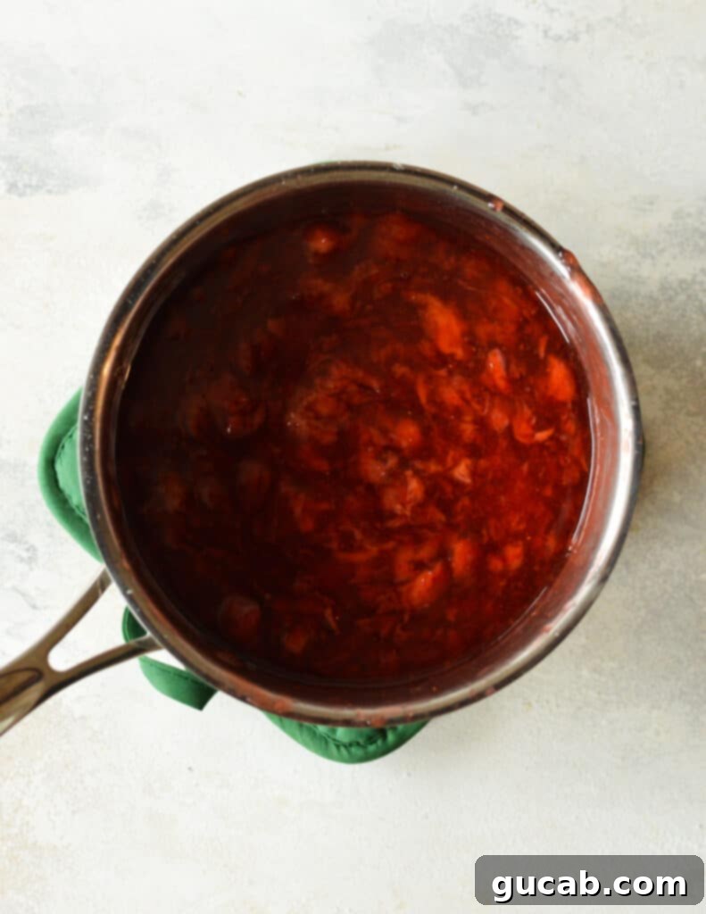 Strawberry filling reaching a thick, jammy consistency in the saucepan after cooking.